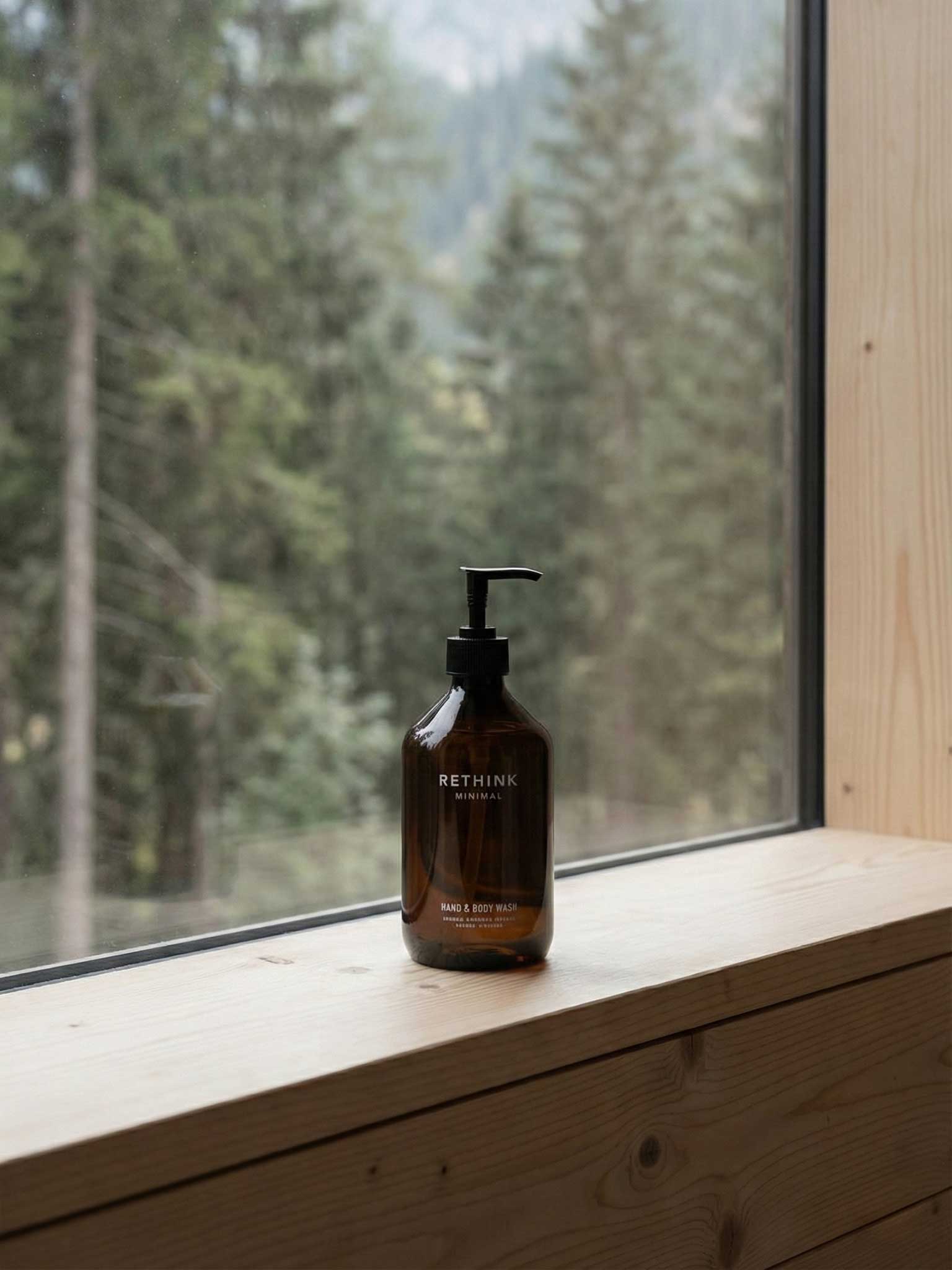 Braune Rethink Minimal rPET Flasche mit Pumpspender für Hand & Body Wash auf einer Holzfensterbank, Waldlandschaft im Hintergrund. Spa Gefühl aus Österreich.